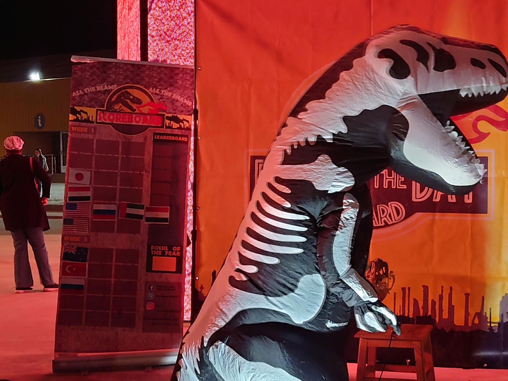 写真)“Five minutes to showtime“と書いたメモを観客に見せて回る化石賞のマスコットである恐竜。主催者自ら言う通り、ショータイムなのだ。