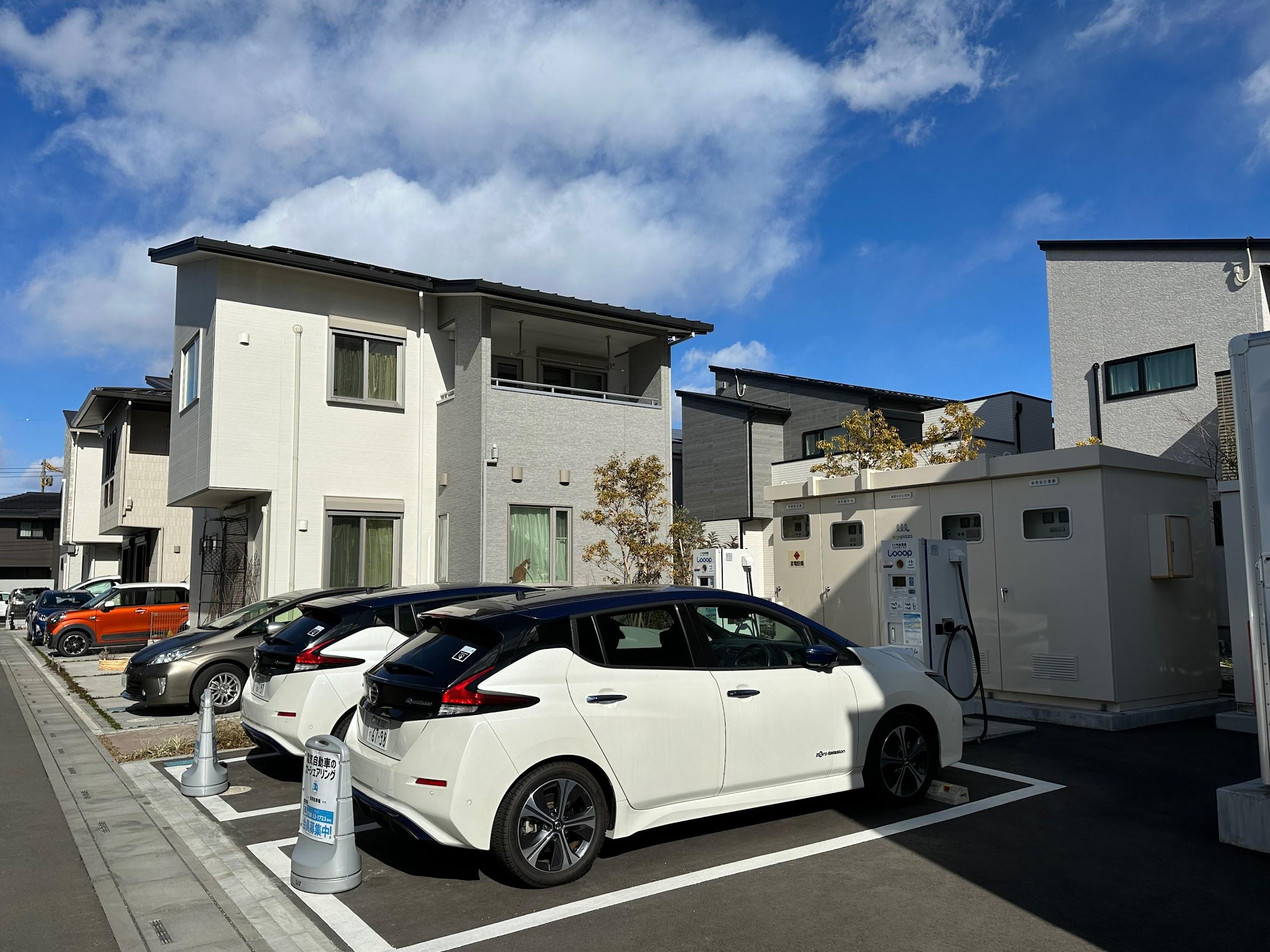 写真)「浦和美園E-フォレスト第3期」内のチャージエリア 2台のEV(日産リーフ)の前にある設備は受変電設備。蓄電池やEV、商用系統からの電気を各住戸へ供給する。カーシェアリング用EV(日産リーフ)は、平日は蓄電池として街区のエネマネに活用(40kWh×2)し、土日はシェアカーとして住民が利用できる。