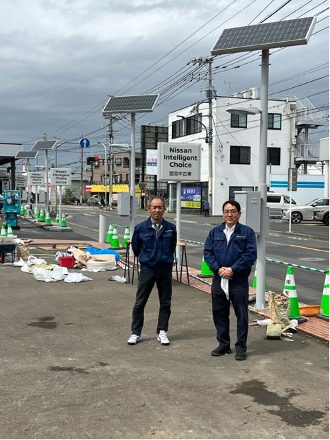 写真)日産東京販売株式会社に納品された非常用蓄電池付き太陽光外灯(4灯) 右が加東社長