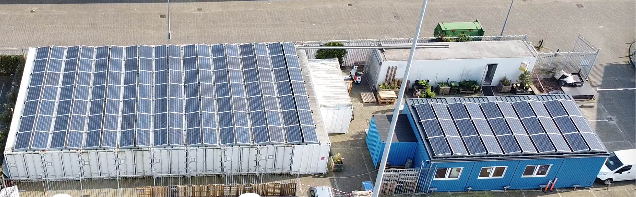 写真)きのこ栽培用コンテナ(左の白い建物)太陽光パネルが屋上に敷き詰められている。