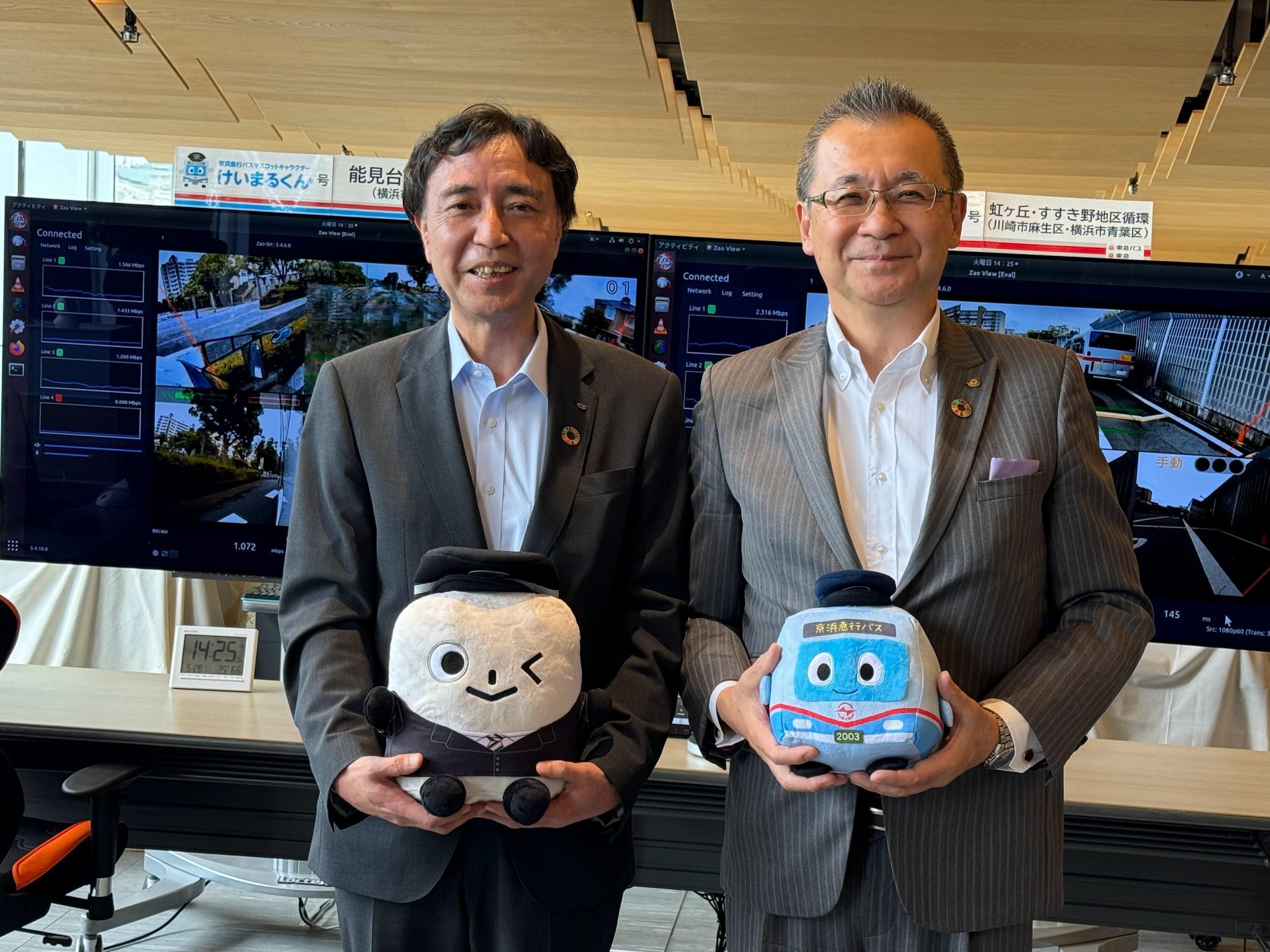 写真)お互いの会社のマスコットを持つ、東急バス古川卓社長(右)と京急バス野村正人社長(左) 2024年5月28日 神奈川県横浜市 京急グループ本社ビルにて