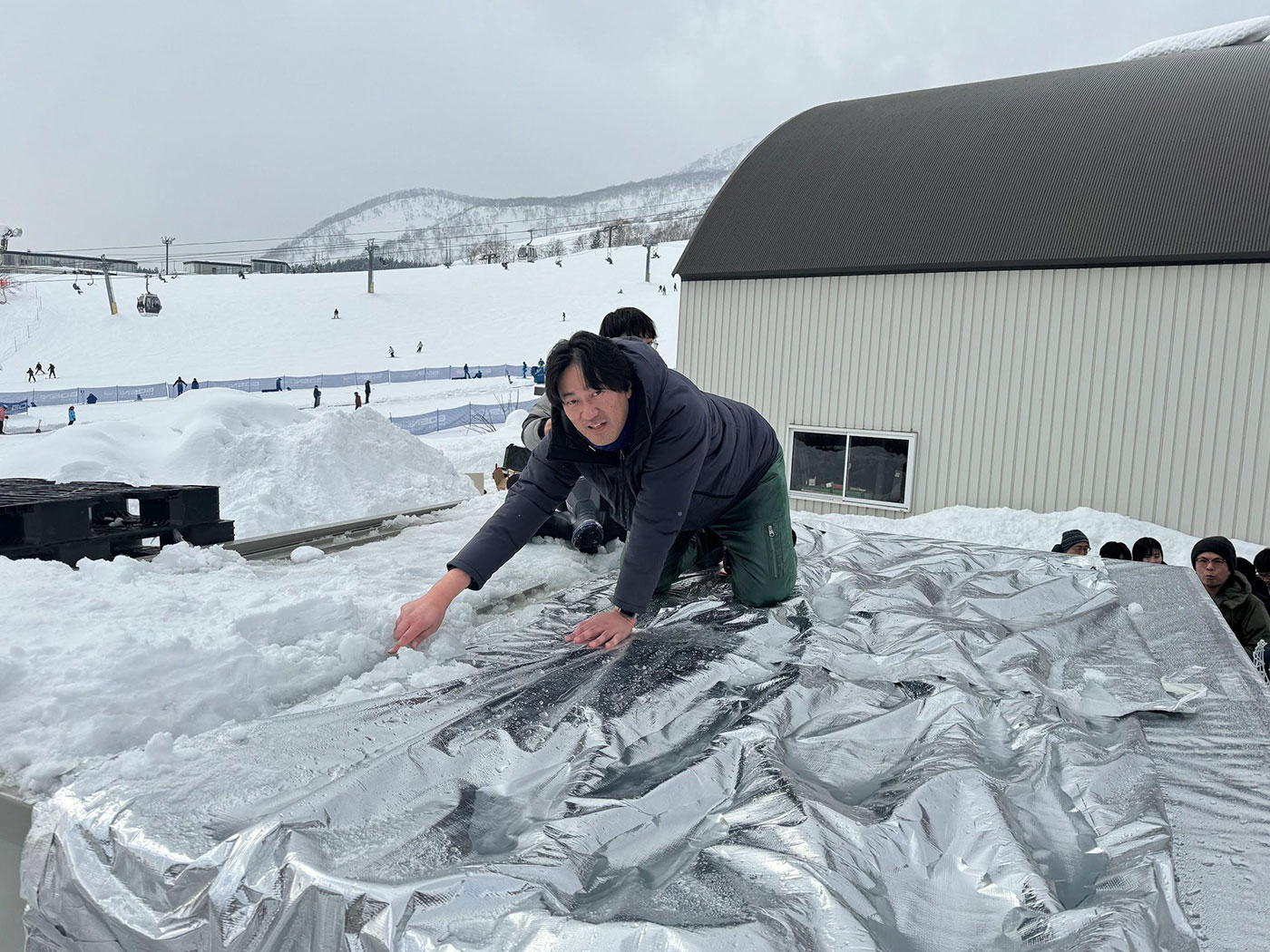 写真)融雪実験用のプレハブの屋根の上でデモンストレーションする電気通信大学榎木光治准教授(2024年1月18日 北海道ニセコにて)